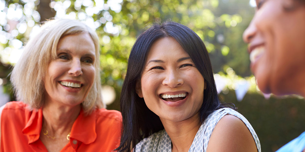 Three women are sitting outdoors, laughing and enjoying a conversation together. 